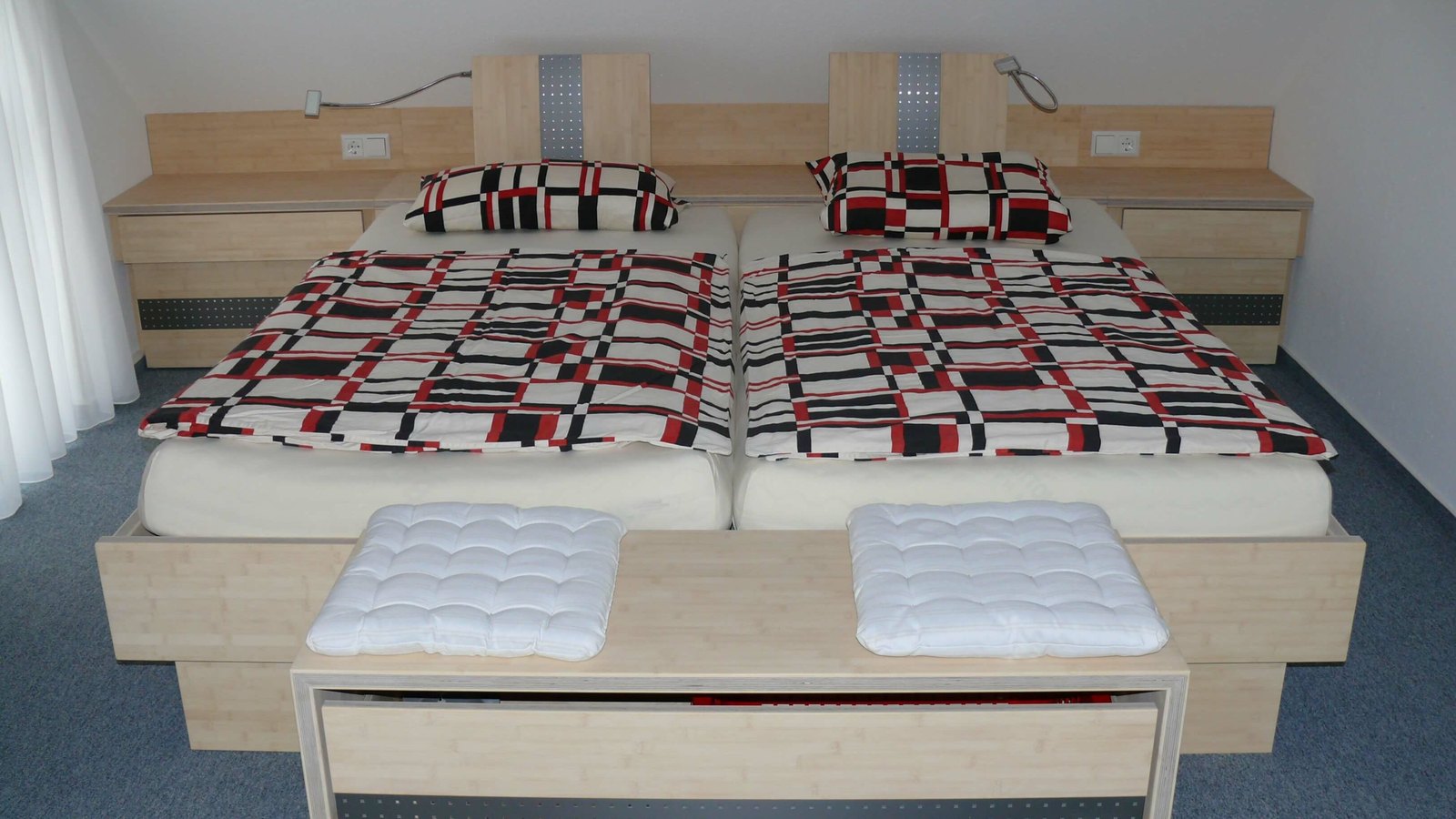 Doppelbett aus hellem Holz mit Kopfteil, seitlichen Nachttischen und einer Bank mit weißen Kissen am Fußende