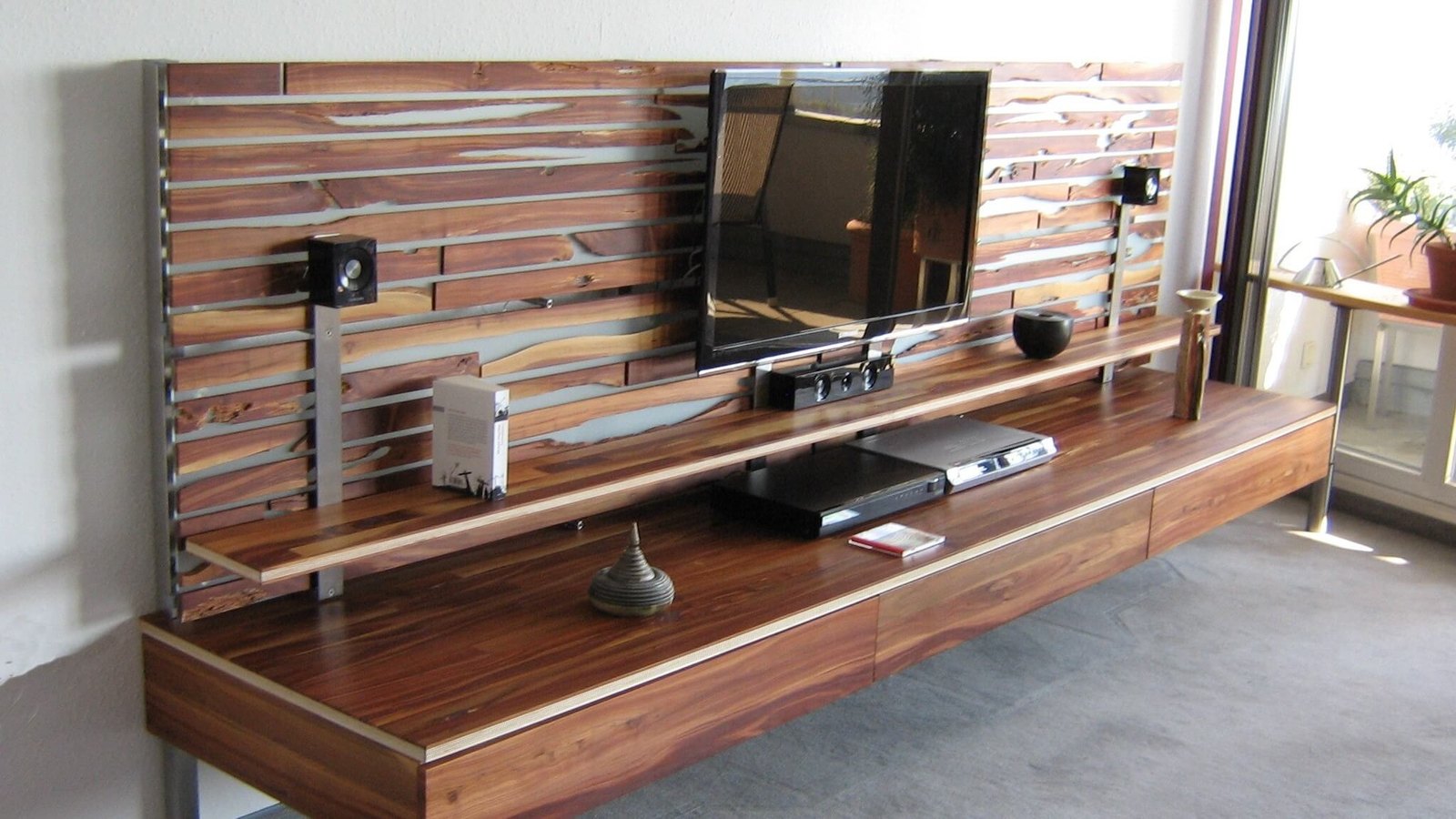 Dunkles Holzpaneel mit Metallstreben als TV-Wand, darunter ein langes, niedriges Sideboard